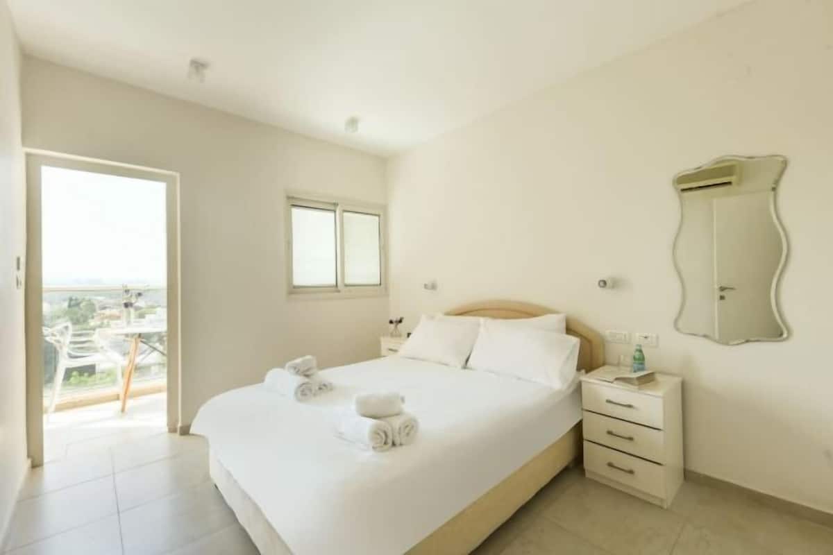 A hotel room with a bed, a bedside table, a mirror, and a balcony with a view.