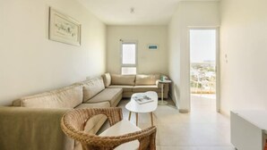 A modern living room with a sofa, a small table, a wicker chair, and a framed picture on the wall. - Skyline 1BR Apartment with City and Sea View (Herzliya)