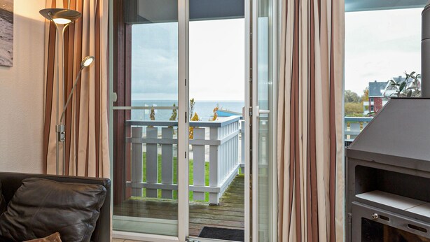 A balcony with a view of the sea, a sliding glass door, a barbecue grill, and a sofa with cushions.