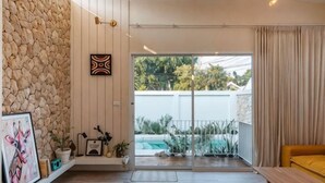 A modern living room with a stone wall, a yellow sofa, a wooden coffee table, and a glass door leading to a balcony. - Wynn resort (Bang Lamung)