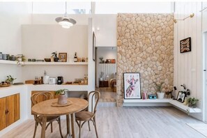 A modern kitchen with a stone wall, wooden cabinets, and a dining area with chairs and a table. - Wynn resort (Bang Lamung)