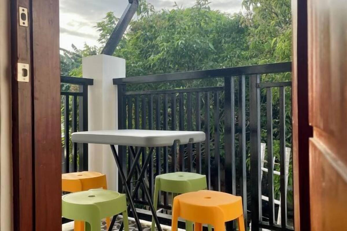 A balcony with a white table and two stools, surrounded by a black railing and greenery.