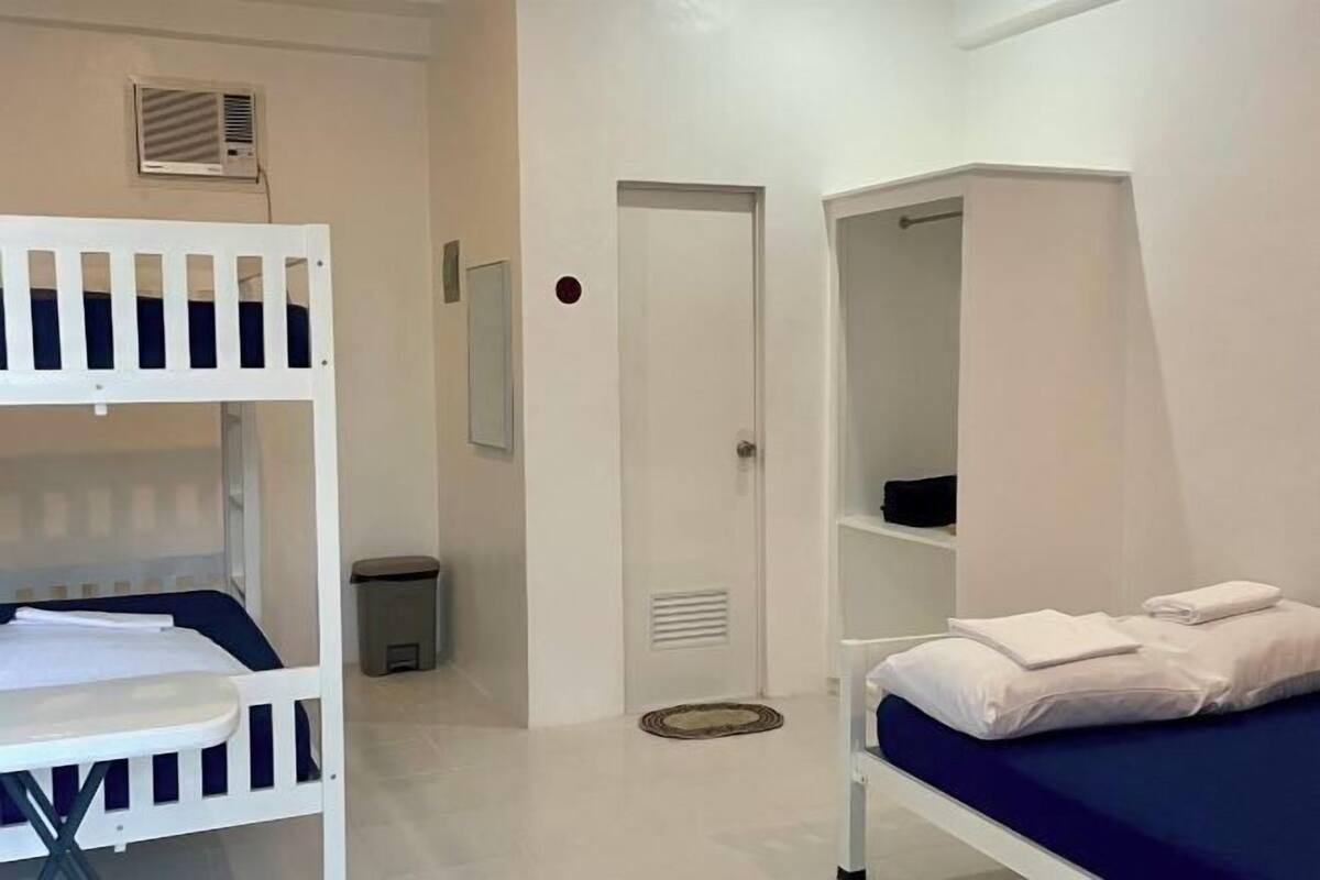 A room with bunk beds, a door, a small trash bin, and a shelf with folded towels.