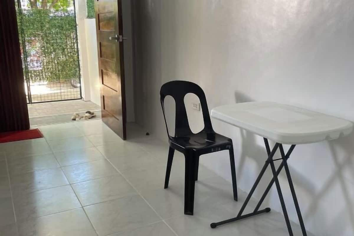 A room with a tiled floor, a black plastic chair, a white table, and a door leading outside.
