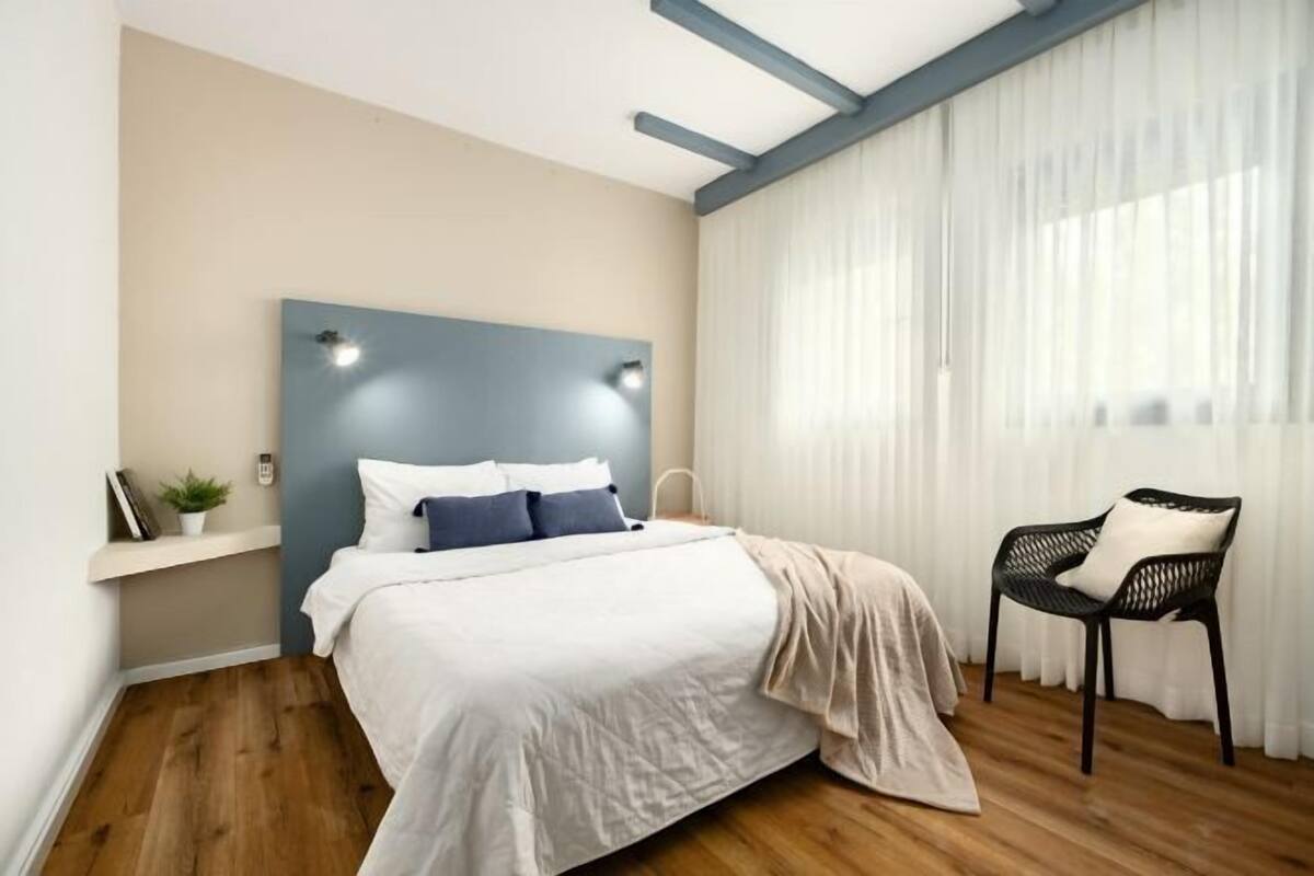 A bedroom with a bed, a nightstand, a chair, and a window with curtains.