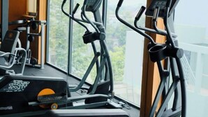Ein Fitnessstudio mit Trainingsgeräten, darunter Laufbänder und Ergometer, mit Blick auf Grünflächen.