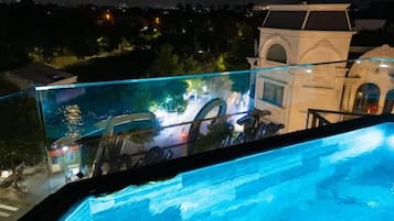 Una piscina con barandilla de cristal que da a un jardín ajardinado y un edificio al fondo.