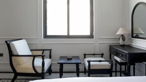 A hotel room with a bed, two armchairs, a small table, a dresser, a mirror, and a window. - The City Boutique Hotel (Bien Hoa)
