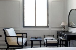 Ein Hotelzimmer mit einem Bett, zwei Sesseln, einem kleinen Tisch, einem Schminktisch und einem Fenster.