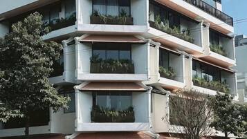 Un edificio de varios pisos con balcones, ventanas y un árbol en primer plano.