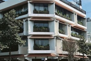 Ein mehrstöckiges Gebäude mit Balkonen, Fenstern und einem Baum im Vordergrund.