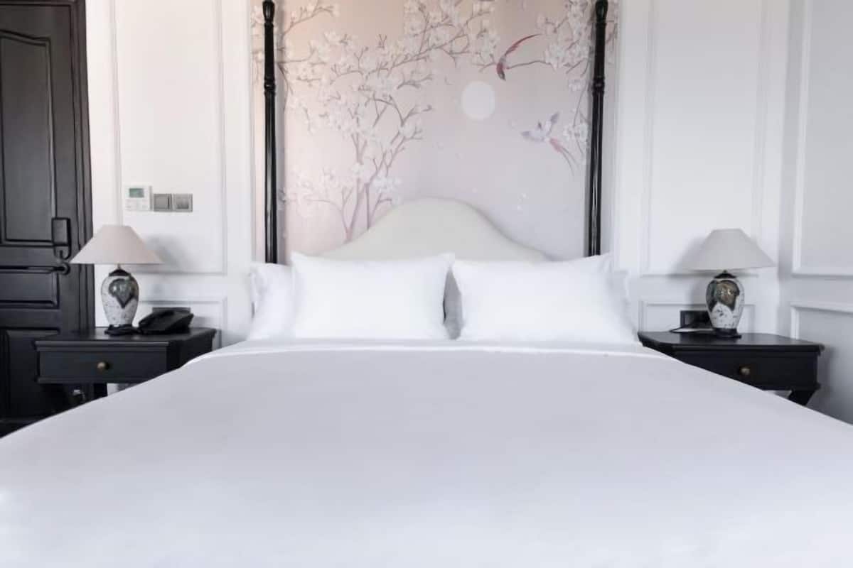 Hotellihuone, jossa on suuri sänky, kaksi yöpöytää valaisimineen, kukka-aiheinen seinämaalaus ja ovi.