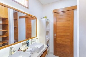 Ein Badezimmer mit einem großen Spiegel, zwei Waschbecken, Holzschränken und einer Holztür.