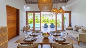 Un comedor con una mesa preparada para cuatro personas, una lámpara de techo de mimbre y vistas a una piscina y follaje.