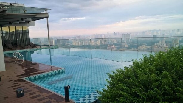 A rooftop infinity pool with a city view, a glass railing, and a wooden deck.
