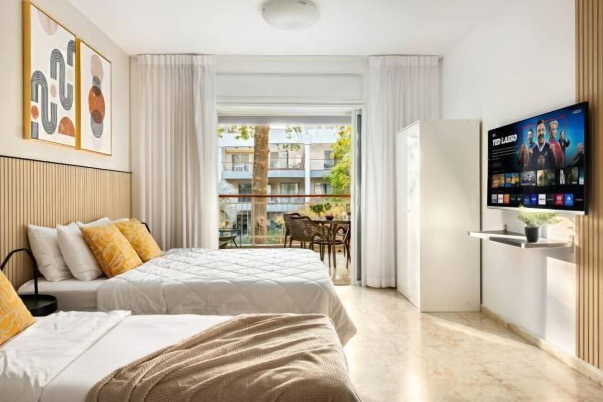 A hotel room with two beds, a TV, and a balcony with a view of the building.