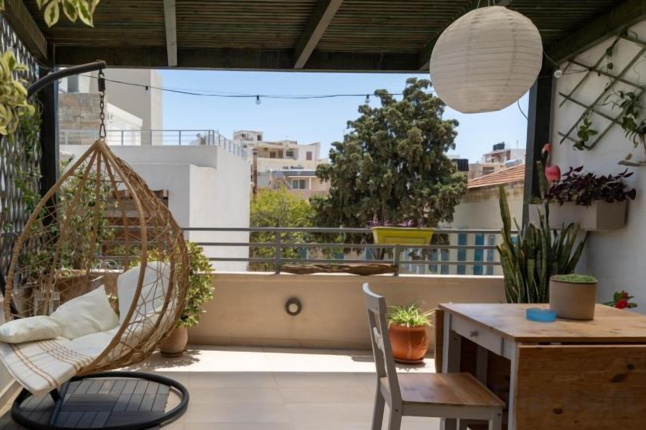 Un balcon avec un fauteuil suspendu, une table et des plantes en pot.