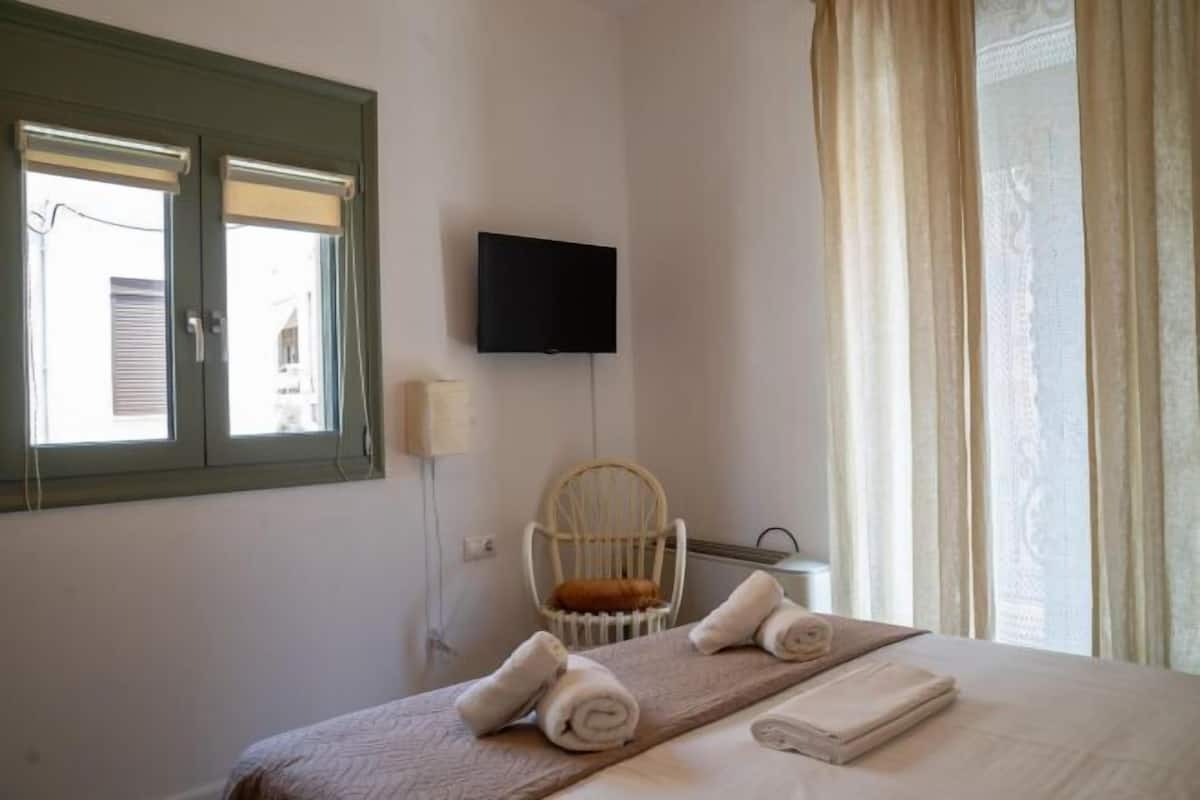 Una habitación de hotel con una cama, una silla, un televisor y una ventana con cortinas.