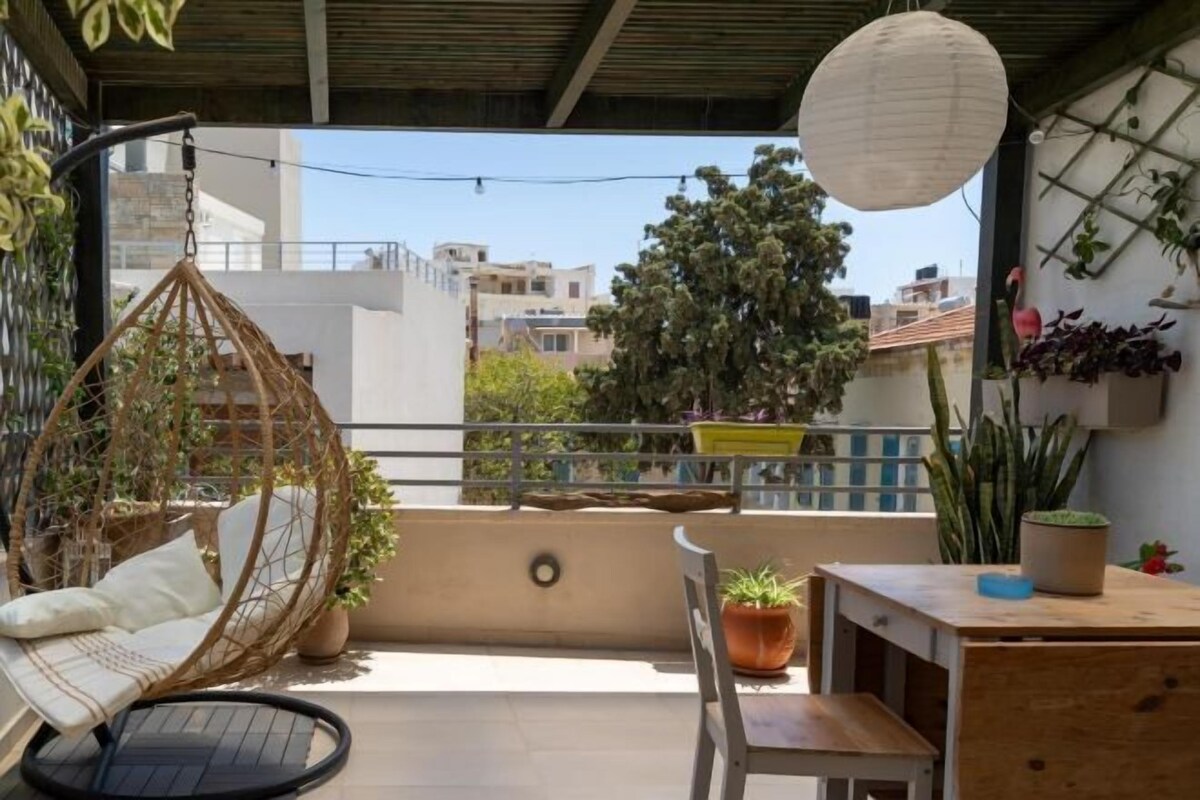 Een balkon met een hangstoel, een tafeltje en planten in potten.