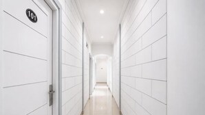 A hallway with white tiled walls and a shiny floor, leading to a door marked with the number 101. - Rays Residence (Jakarta)