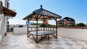 A rooftop terrace with a gazebo, tiled flooring, and a view of surrounding buildings. - Rays Residence (Jakarta)