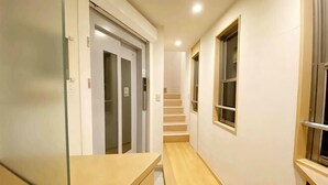 A narrow hallway with a wooden floor, a glass door, a staircase, and a window. - SunStay Fudomae I（601） (Tokyo)