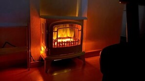 A wood-burning stove with a visible fire, a chair in front, and a window to the left. - SunStay Fudomae I（601） (Tokyo)
