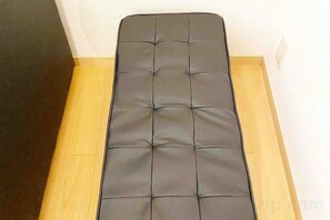 Un banc noir rembourré, doté d’un motif capitonné, est placé sur un plancher en bois, adossé à un mur blanc.