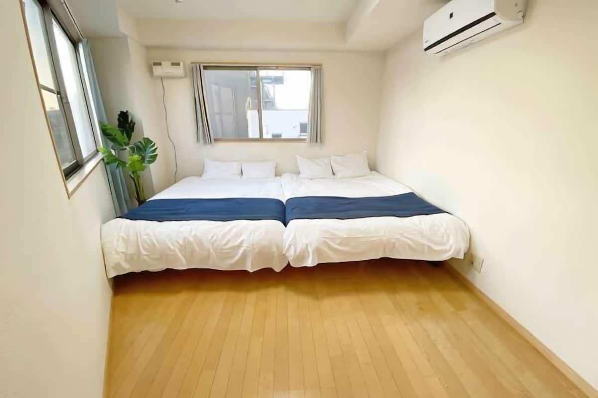 A room with a double bed, a window, and an air conditioning unit.