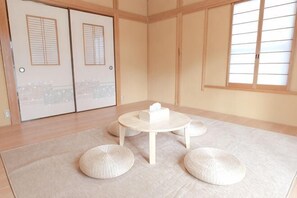 Ein Zimmer mit Tatami-Böden, einem niedrigen Tisch mit einem weißen Block und einem Fenster mit Holzrahmen.
