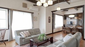 A living room with a sofa, coffee table, and a dining area with chairs. - Private Villa Izu Omuro Kogen (Ito)
