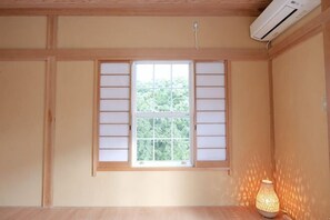 Ein Zimmer mit Fenster zur Shoji-Schirmkonstruktion, Holzwänden, einem Deckenventilator und einer Stehlampe.
