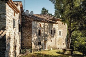Un edificio de piedra con techo de tejas, un banco de madera y un árbol al fondo.
