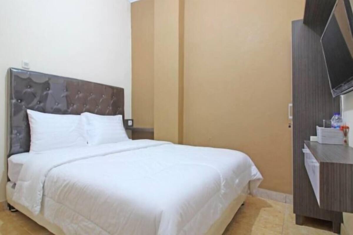 A hotel room with a bed, a TV mounted on the wall, and a desk with a chair.