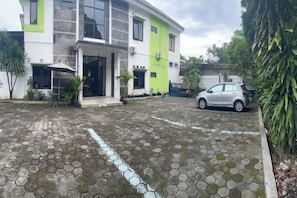 A building with a green and white facade, a paved entrance area, and a parked car. - RedDoorz at Greenhouse Tegalwaras Palagan (Ngaglik)
