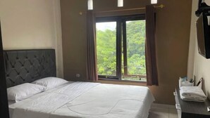 Quarto de hotel com cama, janela com cortinas, televisão e pequena mesa com toalhas.