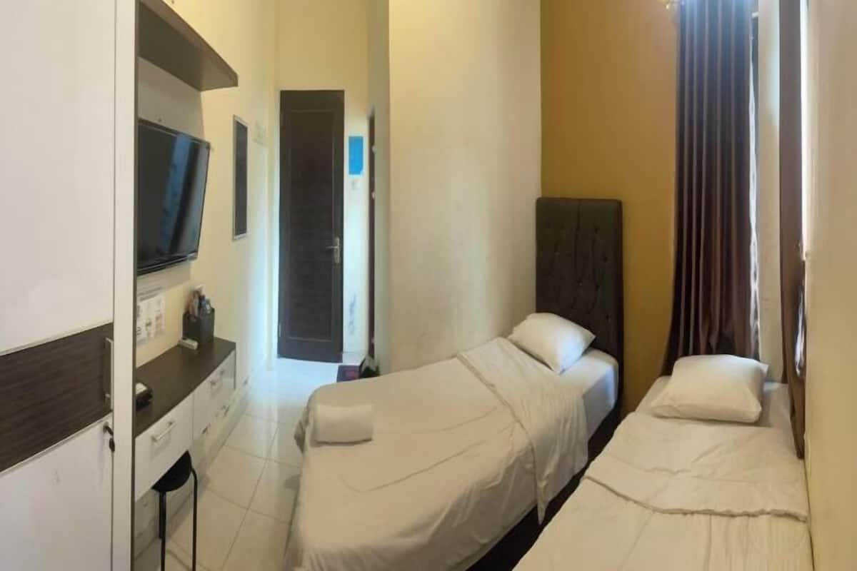 A hotel room with two single beds, a small desk with a chair, a television, and a door leading to another room.