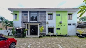 Um edifício de dois andares com entrada em azulejos, um carro vermelho estacionado em frente e uma pequena área externa com plantas.
