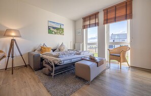 A bedroom with a bed, bedside table, lamp, and a view of the outside.