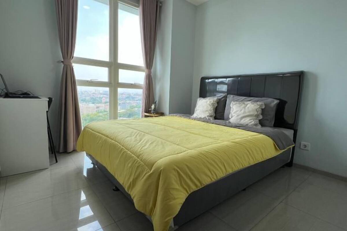 Un dormitorio con cama, mesita de noche, lámpara y ventana con cortinas.