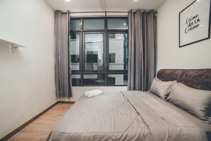 Een slaapkamer met een groot bed, een raam met gordijnen, een citaat in een lijst op de muur en een houten vloer.