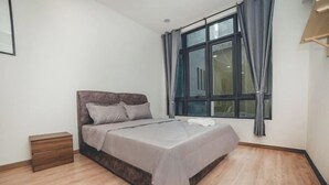 Een slaapkamer met een bed, nachtkastje, raam met gordijnen en een houten vloer.