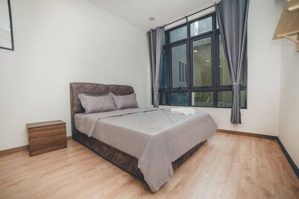 Une chambre à coucher avec un lit, une table de chevet, une fenêtre avec des rideaux et un plancher en bois.