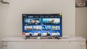 Een flatscreen-tv aan een witte muur, waarop een streamingdienst interface met verschillende filmminiatuurafbeeldingen te zien is.