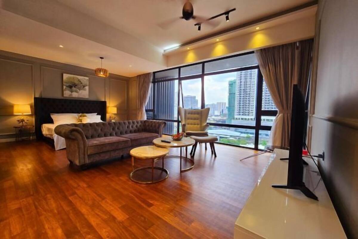 A modern hotel room with a large bed, a sofa, two round tables, and a TV.