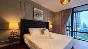 A hotel room with a large bed, two bedside lamps, a plush headboard, a city view, and a decorative ceiling light. - Anggun KLCC 1BR @KL City monorail Netflix 1CP (Kuala Lumpur)