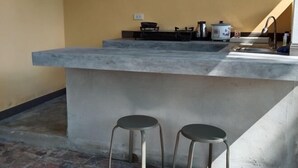 Une cuisine avec un îlot central en béton, deux tabourets, un évier et une cuisinière.
