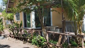 Un bâtiment à la façade jaune, doté de grandes fenêtres et d’une clôture en bois ornée de plantes.
