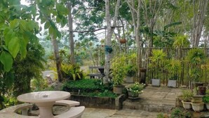 A garden patio with a round table and benches, surrounded by potted plants and trees. - Baan Namthip Homestay Trang บ้านน้าทิพย์ โฮมสเตย์ตรัง (Sikao)