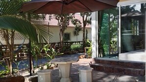 Une terrasse extérieure avec une table et des chaises en pierre, entourée de plantes et d’une clôture en bois.